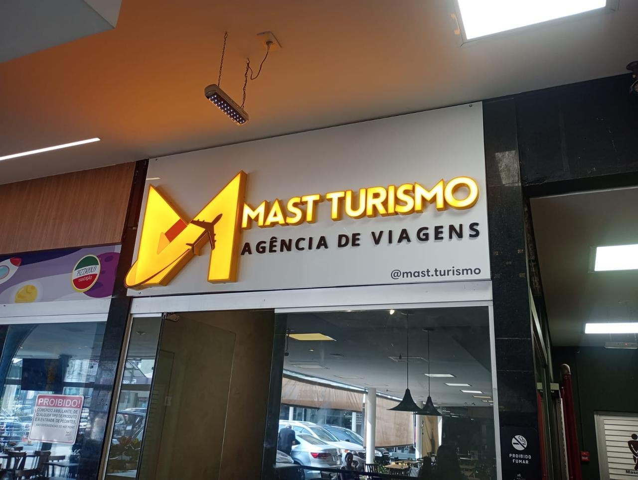Letreiro iluminado da Mast Turismo aplicado em painel branco.