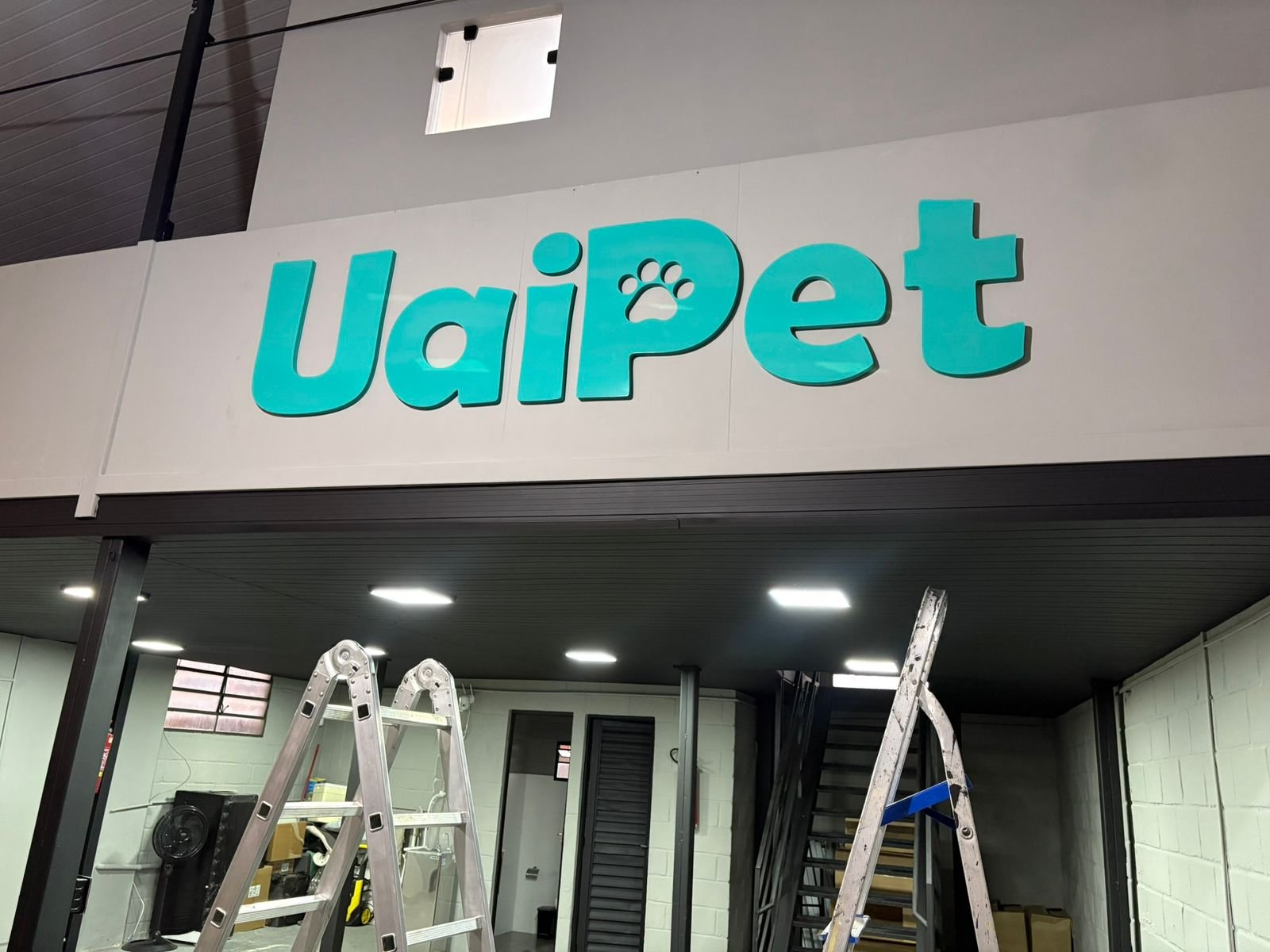 Letreiro externo da UaiPet em azul turquesa instalado em estrutura interna durante a montagem.